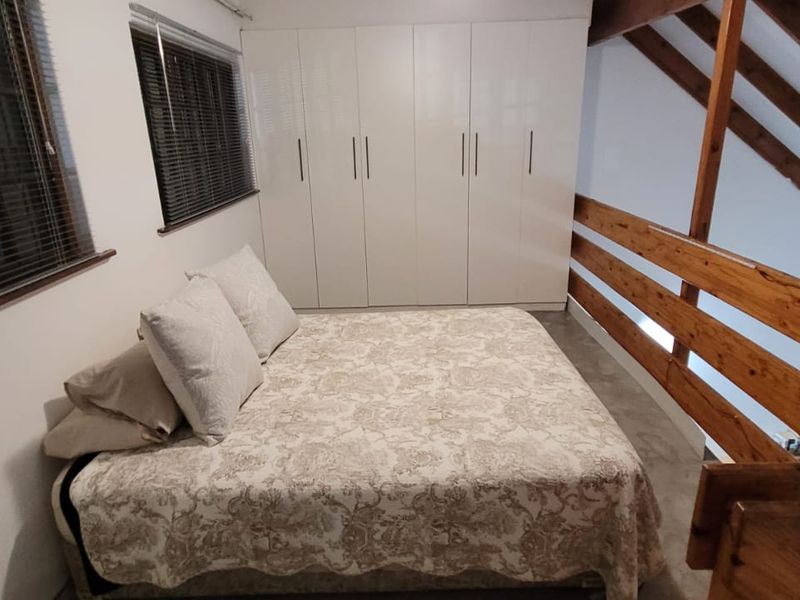 Loft-style bedroom featuring exposed timber rafters, a wooden balustrade, and modern white built-in cupboards.