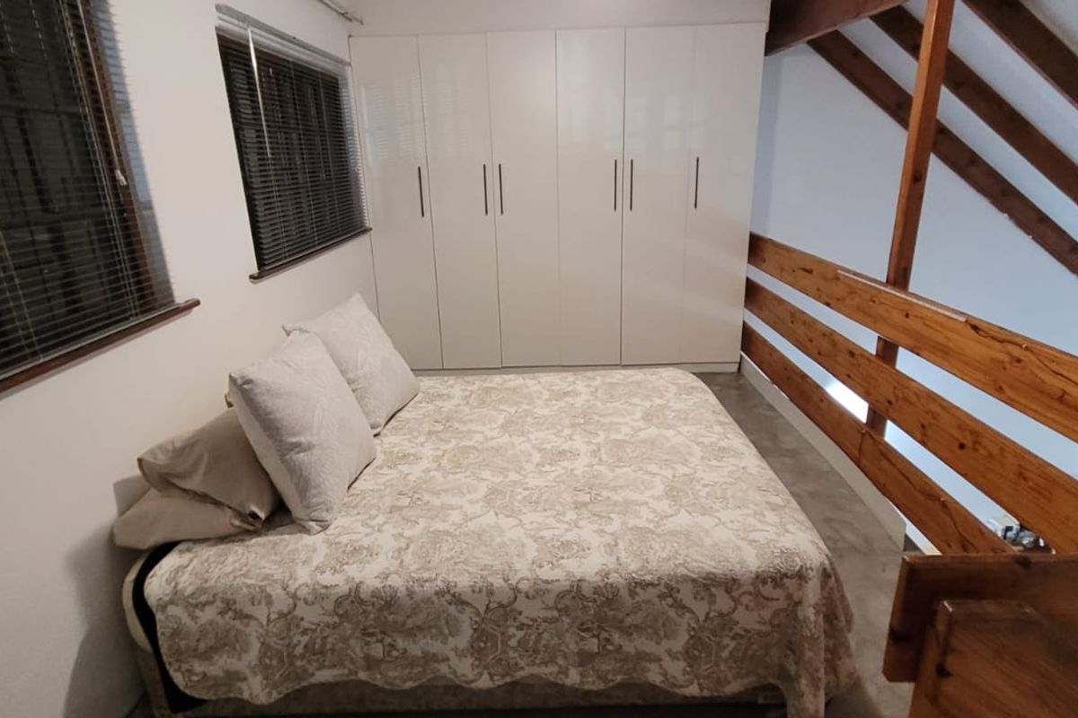 Loft-style bedroom featuring exposed timber rafters, a wooden balustrade, and modern white built-in cupboards.