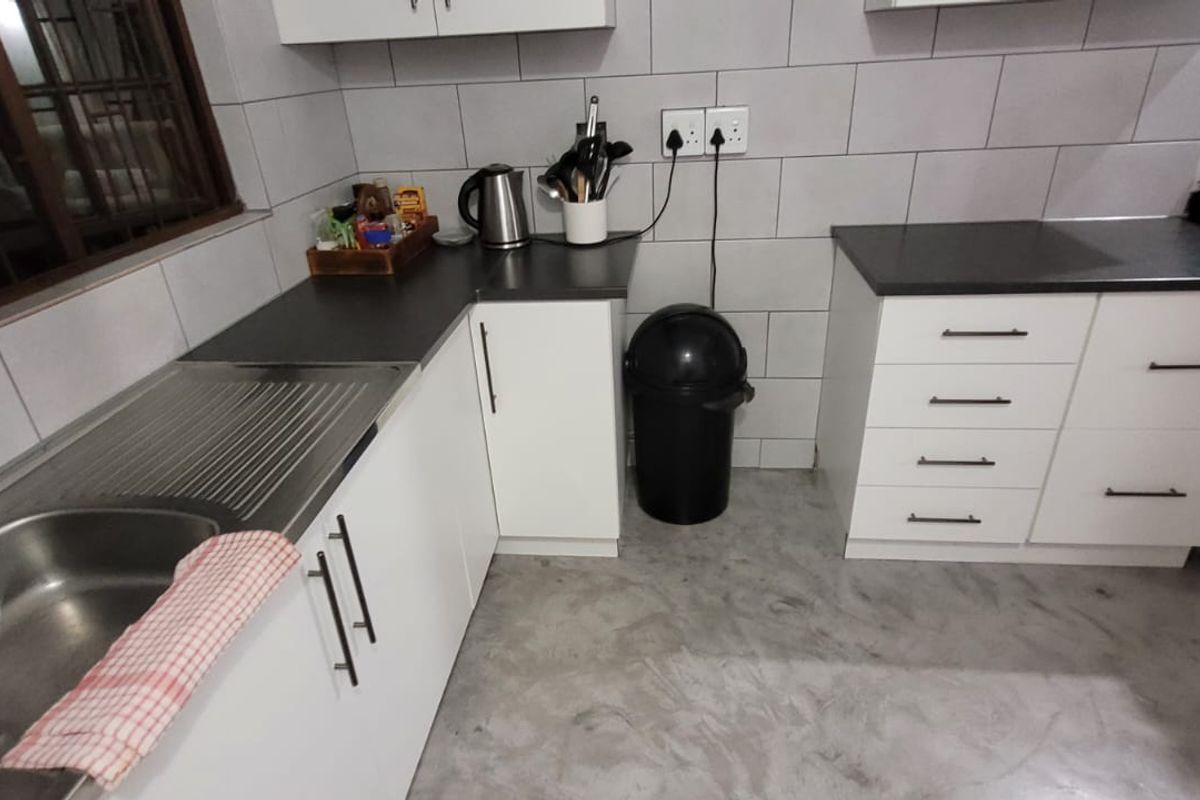 A functional kitchen featuring white cabinetry, dark laminate countertops, tiled backsplash, and polished concrete flooring with a stainless steel sink.