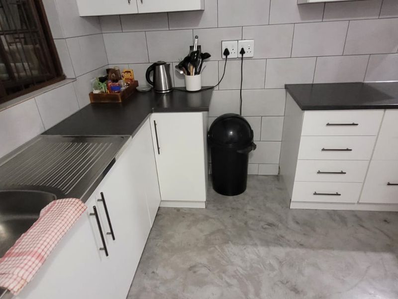 A functional kitchen featuring white cabinetry, dark laminate countertops, tiled backsplash, and polished concrete flooring with a stainless steel sink.