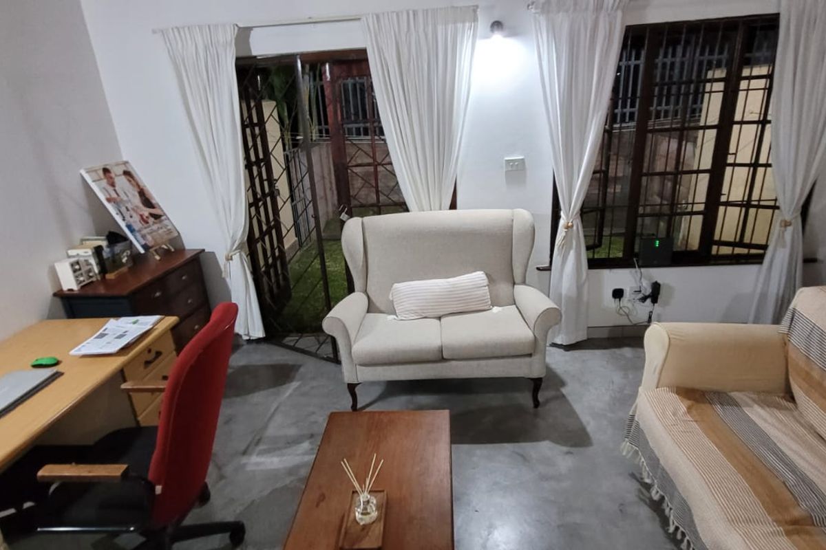 A living room area featuring concrete flooring, security bars on windows, and a sliding glass door providing access to the exterior.