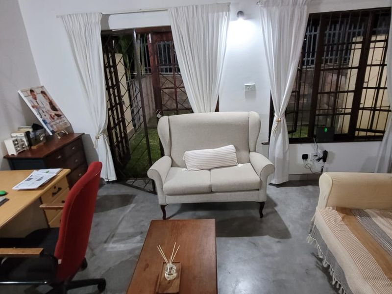 A living room area featuring concrete flooring, security bars on windows, and a sliding glass door providing access to the exterior.