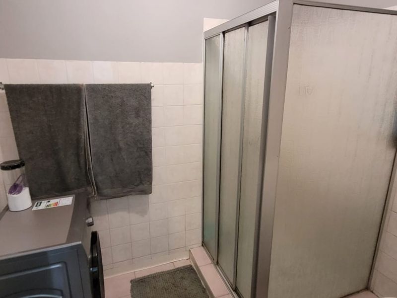A functional bathroom featuring a shower enclosure with sliding doors, tiled wall finishes, and a window with security bars.