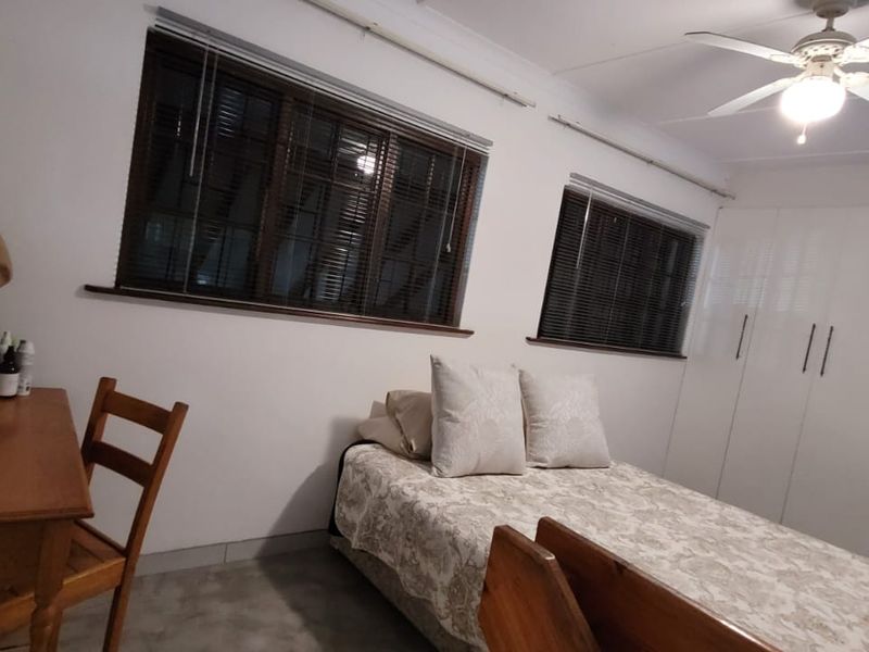 A bedroom featuring built-in cupboards, a ceiling fan, and venetian blinds, providing a functional and well-lit sleeping space.