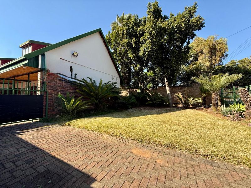 Front exterior view featuring a brick driveway, landscaped garden area, and secure gated entrance with established trees and boundary walling.