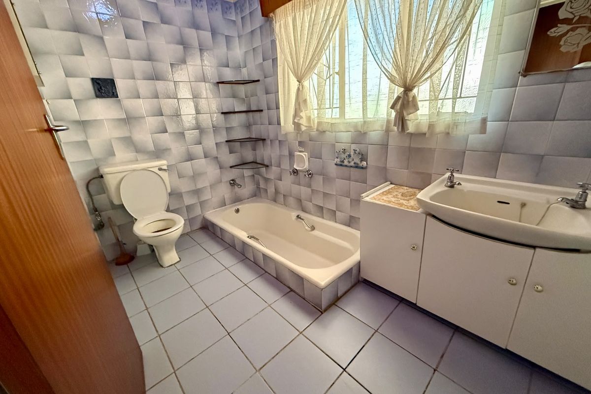 A functional bathroom featuring a built-in bathtub, vanity cabinet with basin, and toilet, finished with dated wall and floor tiling.