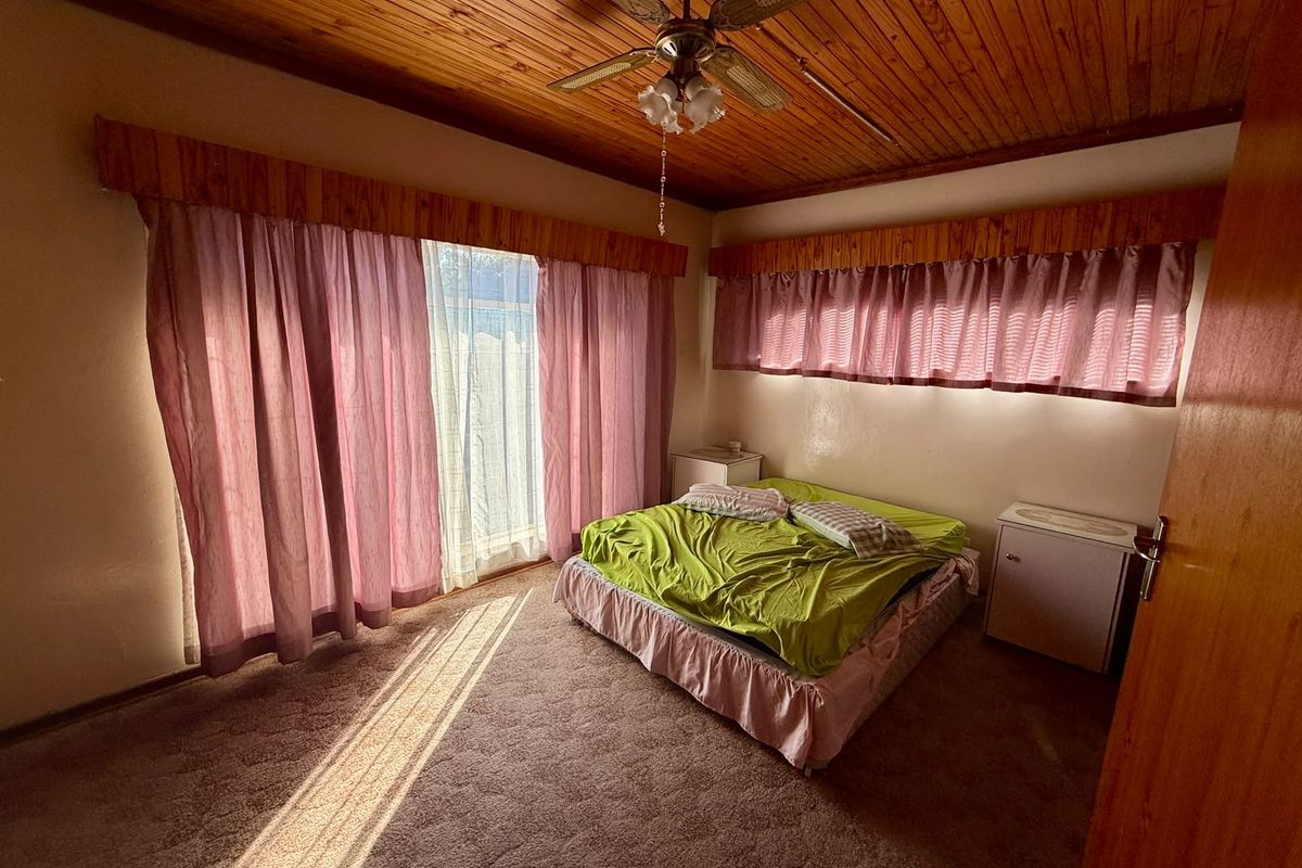 A bedroom featuring a timber-clad ceiling with a central fan and carpeted flooring, offering a dated aesthetic ready for modernization.