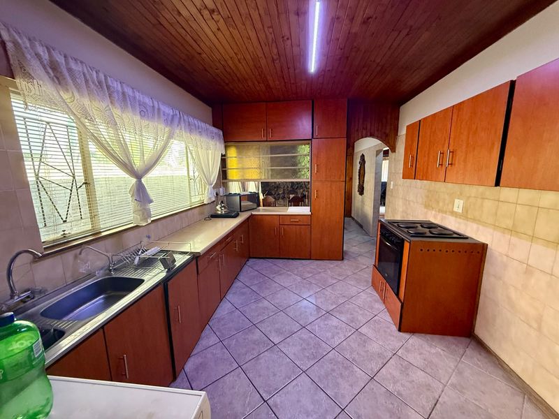A functional kitchen featuring wooden cabinetry, tiled flooring, a timber ceiling, and a built-in sink area with a tiled backsplash.