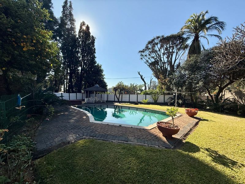 A private outdoor pool area featuring a swimming pool, brick paved surround, and a gazebo set within a landscaped garden.