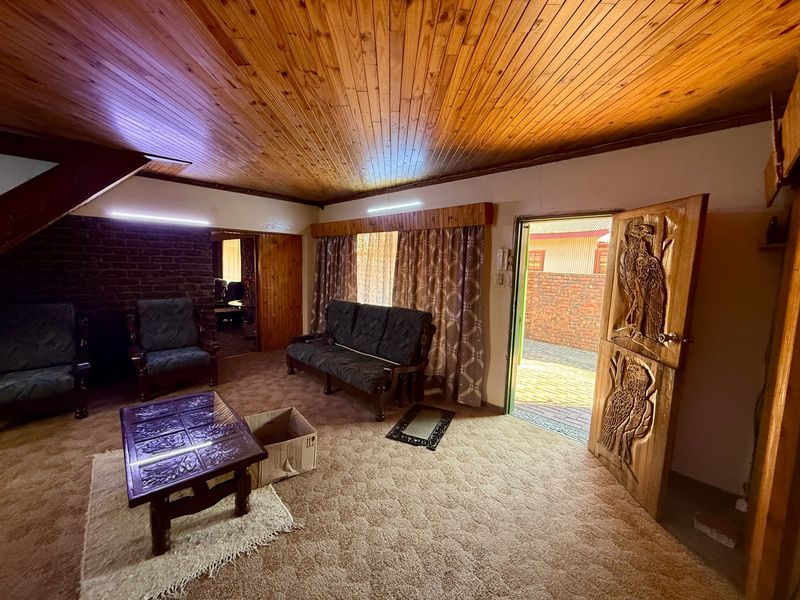 Living room featuring a timber tongue and groove ceiling, exposed brick wall, and a unique carved wooden door leading to the exterior.