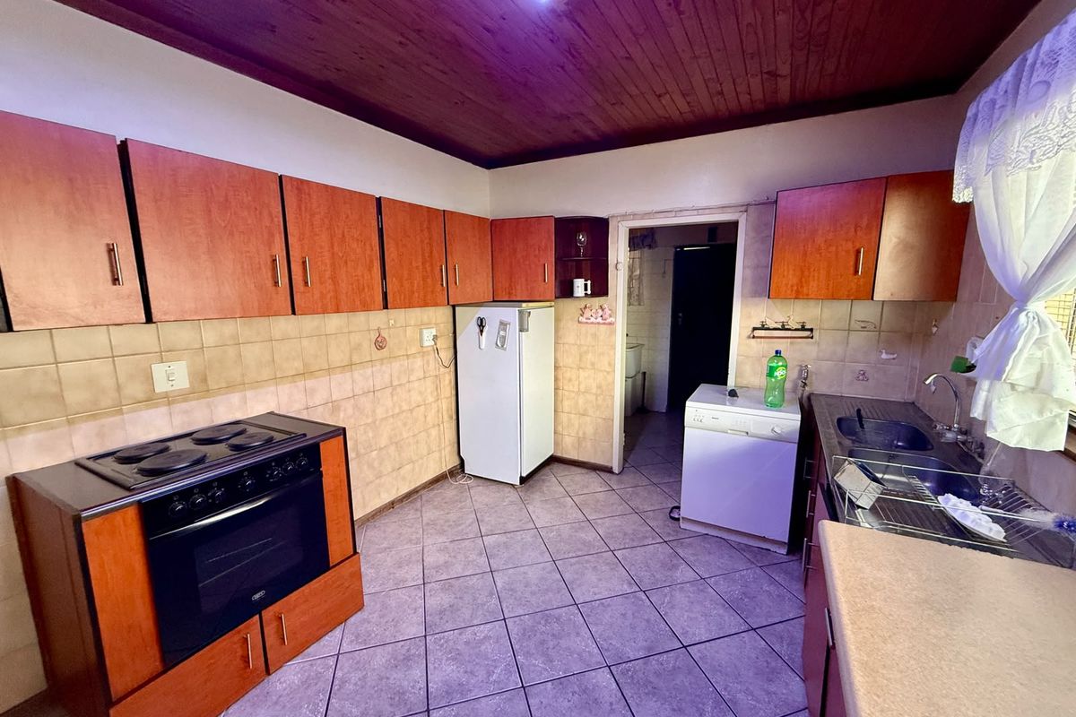 A dated kitchen featuring timber ceilings, tiled flooring, built-in cabinetry, and a freestanding stove, offering potential for a modern renovation.