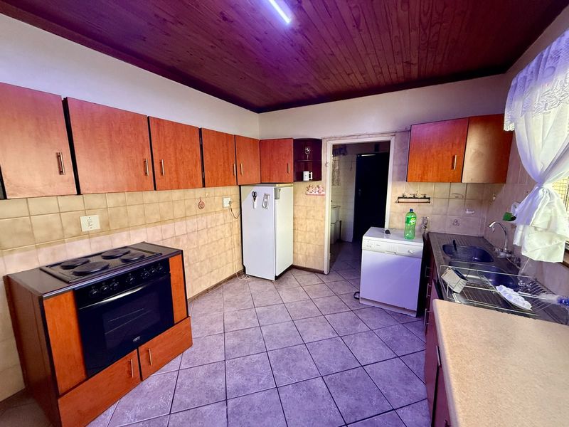 A dated kitchen featuring timber ceilings, tiled flooring, built-in cabinetry, and a freestanding stove, offering potential for a modern renovation.