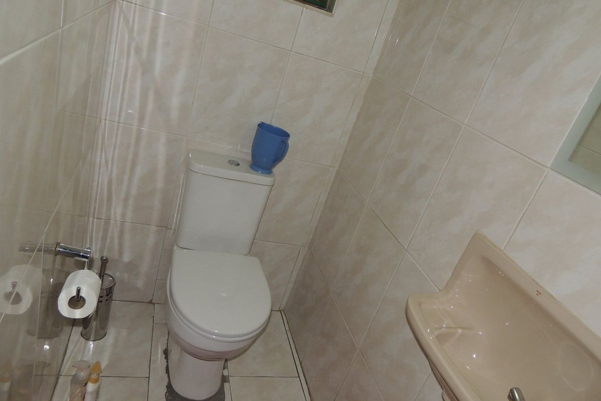 A compact bathroom featuring a standard toilet and wall-mounted basin with neutral ceramic wall and floor tiling.