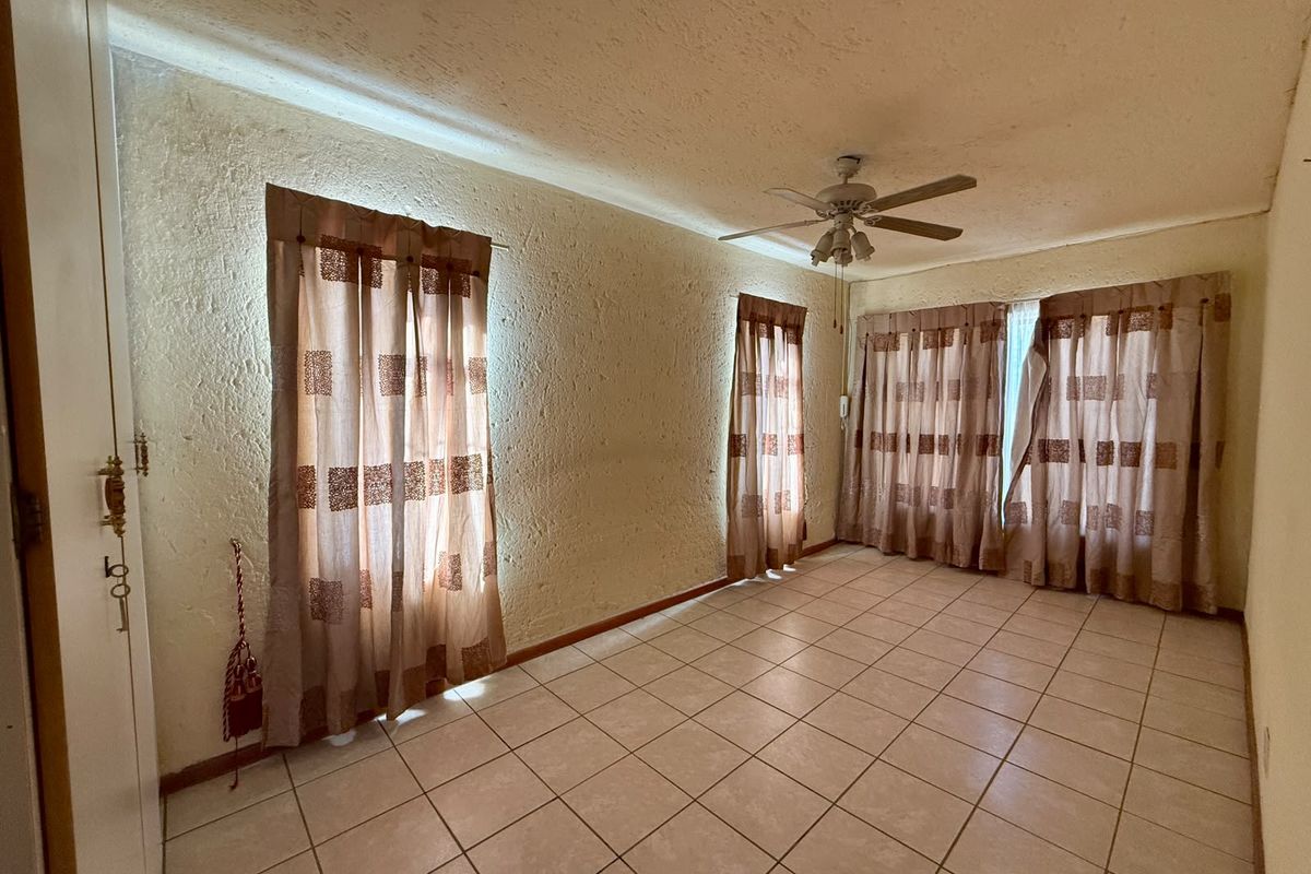 An empty bedroom featuring tiled flooring, a ceiling fan, and built-in cupboard storage with textured wall finishes.