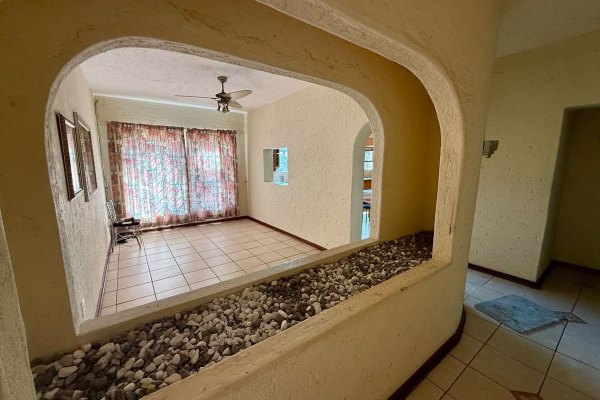 An empty living area featuring tiled flooring, a ceiling fan, and a unique arched opening with a built-in stone planter box.