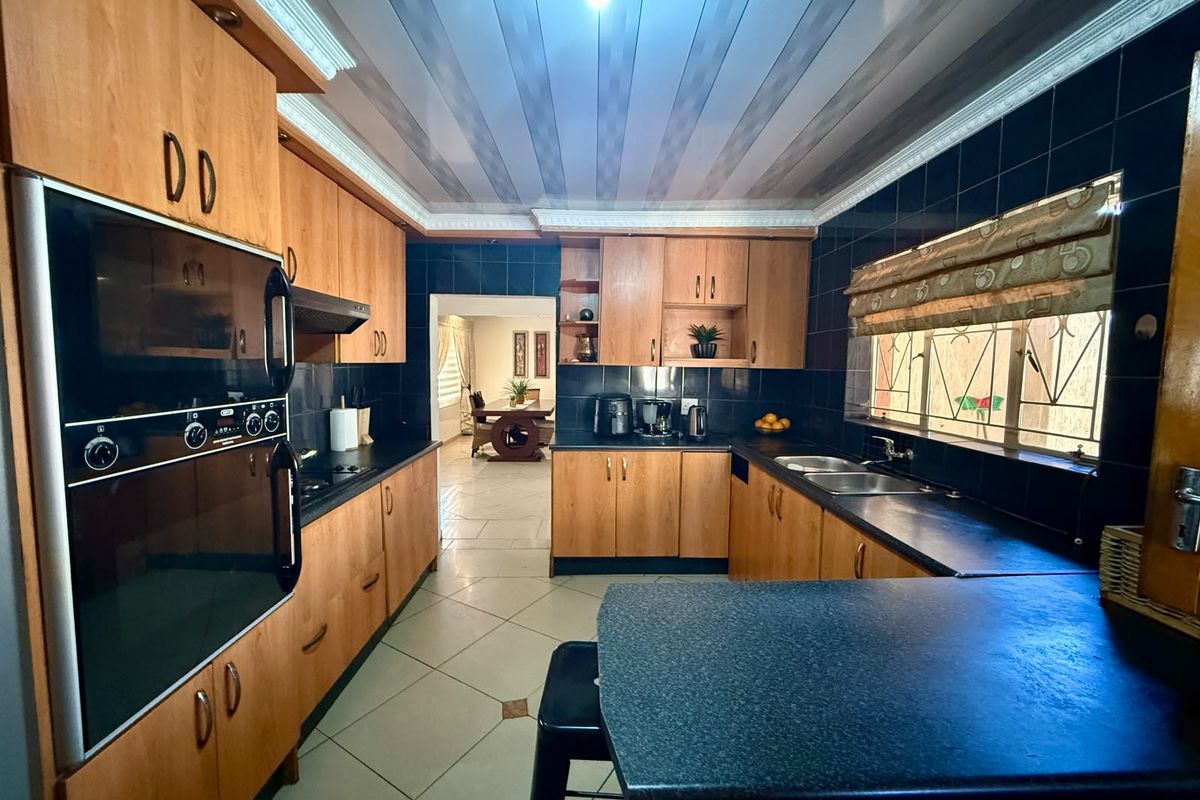 A functional kitchen featuring wood-finish cabinetry, dark countertops, a built-in oven, and tiled finishes, with an open flow into the adjacent dining area.