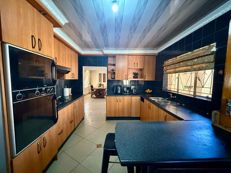 A functional kitchen featuring wood-finish cabinetry, dark countertops, a built-in oven, and tiled finishes, with an open flow into the adjacent dining area.