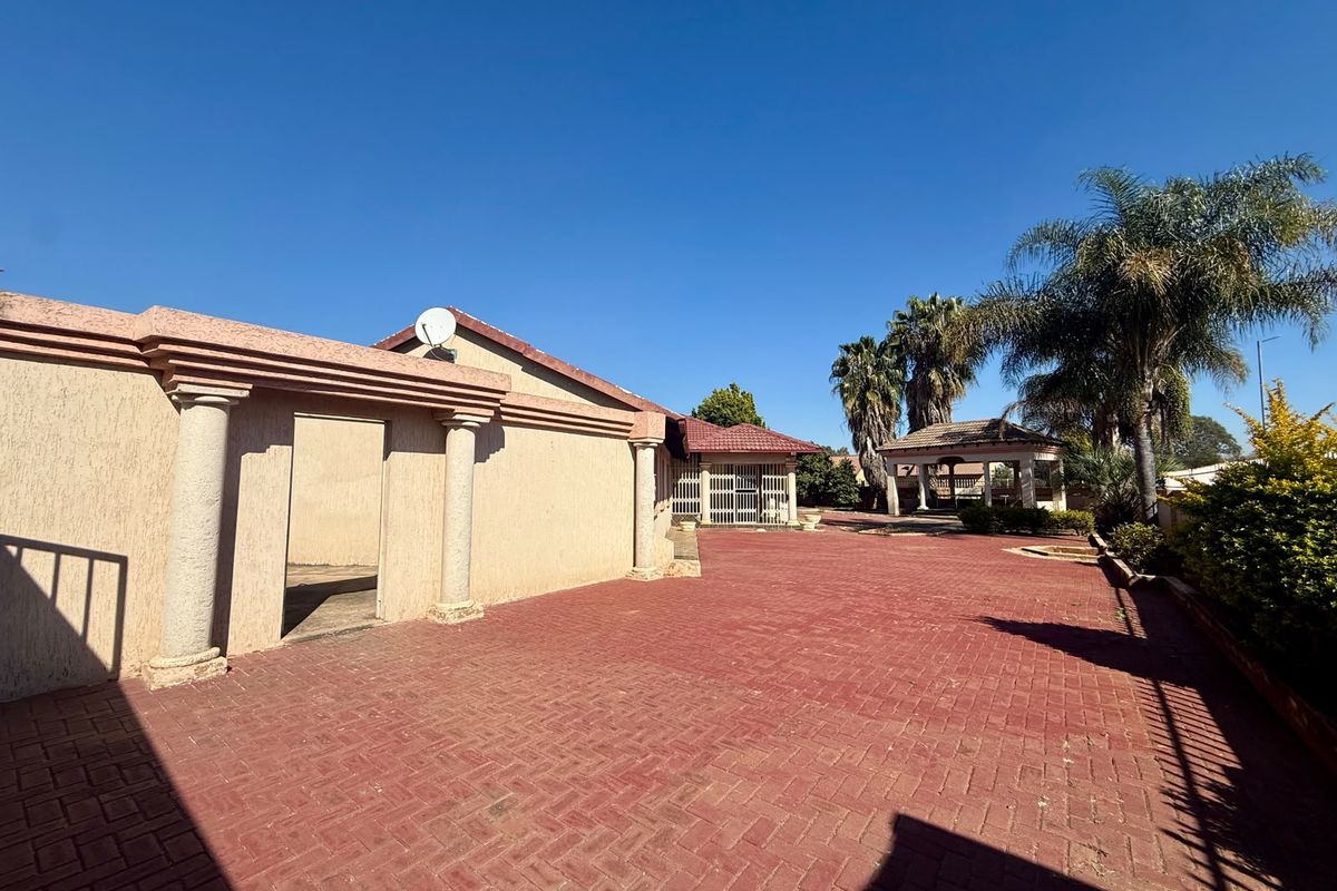 Spacious rear courtyard featuring red brick paving, decorative architectural columns, and a detached gazebo structure in the garden area.