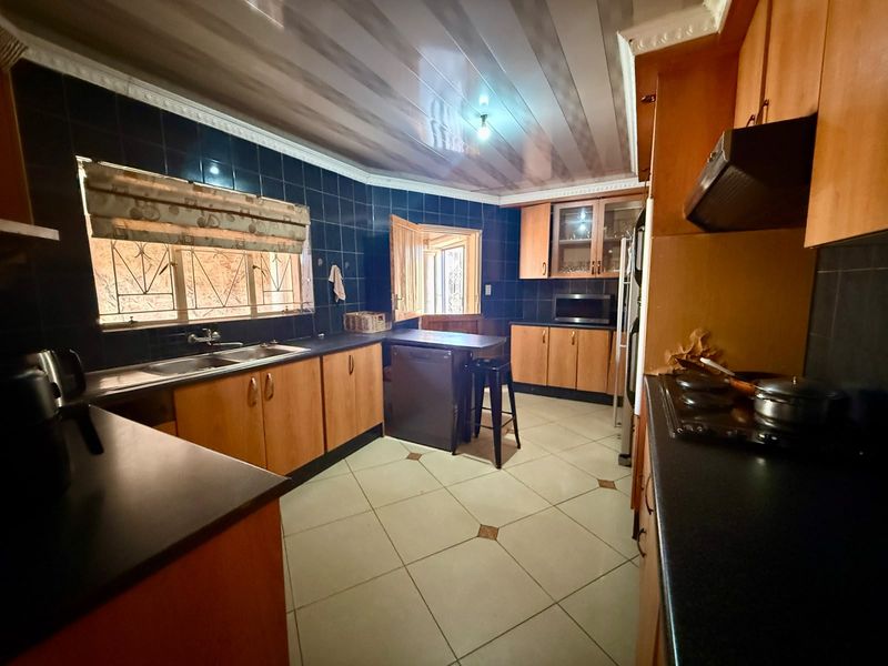 A functional kitchen featuring wooden cabinetry, dark countertops, tiled splashbacks, and ceramic flooring, offering a practical layout with ample storage space.