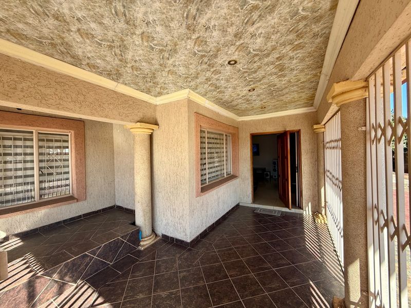 A covered patio area featuring tiled flooring, decorative ceiling finishes, and structural columns, providing a sheltered entrance to the home.