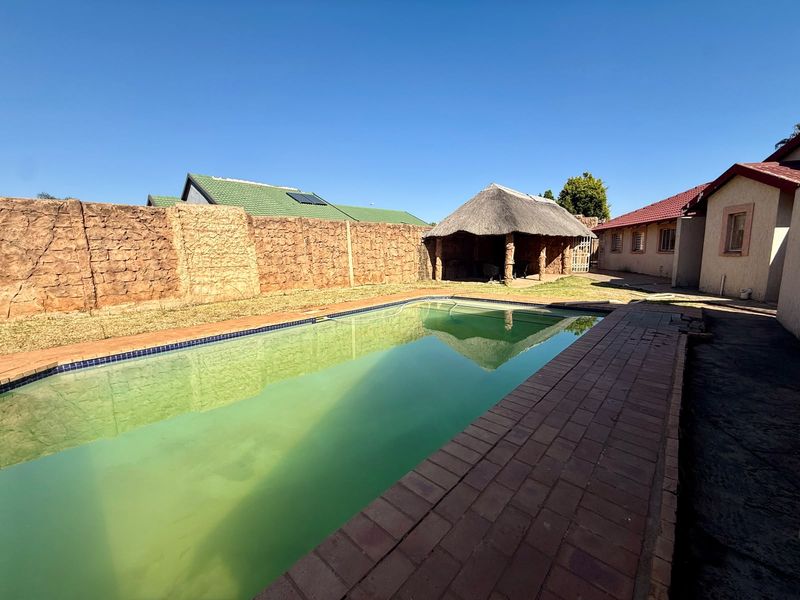 Outdoor pool area featuring a swimming pool, paved surround, and a traditional thatched lapa structure set against a boundary wall.