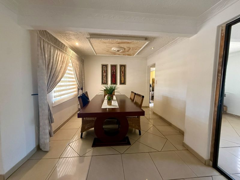 A dining room featuring ceramic floor tiles, a decorative recessed ceiling panel with downlights, and coving.