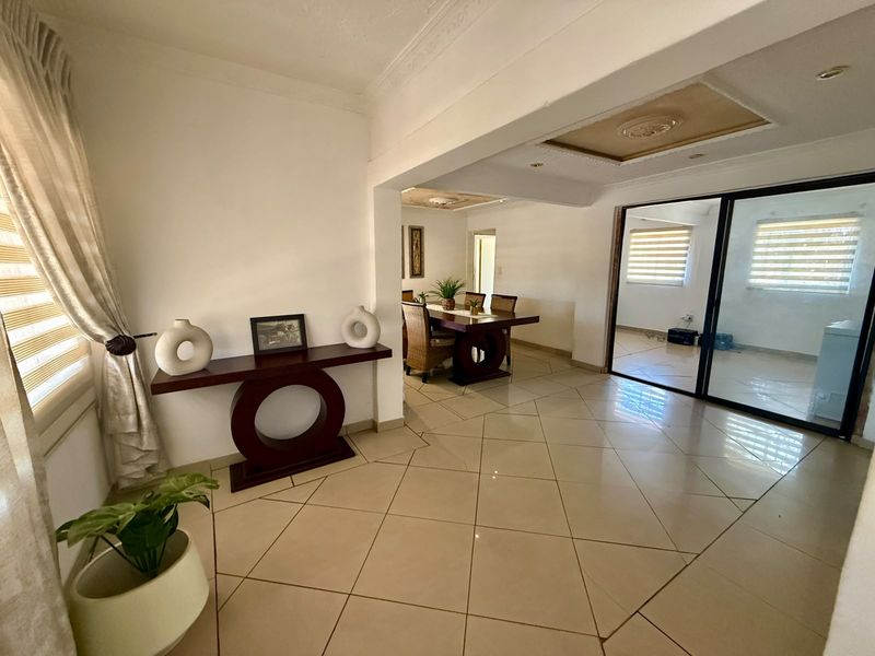 Spacious open-plan living and dining area featuring large format floor tiles, decorative ceiling details, and sliding glass doors leading to an adjacent space.
