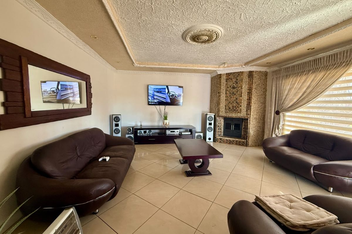 Spacious living room featuring tiled flooring, a decorative ceiling rose, and a unique corner fireplace with stone cladding.