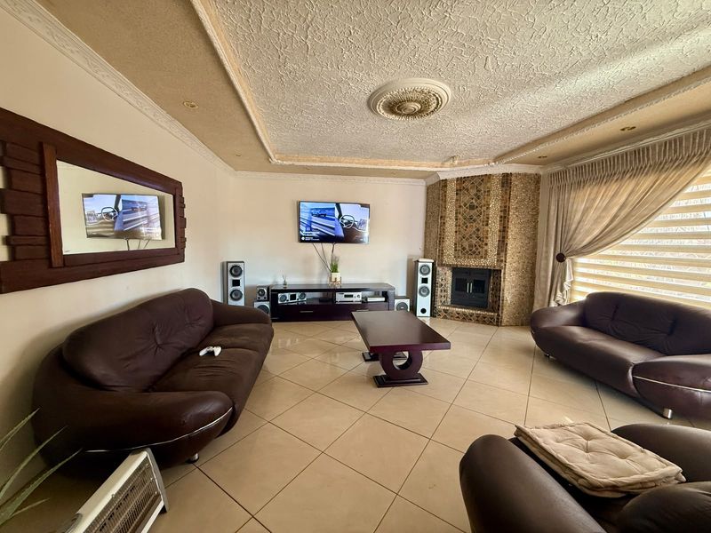 Spacious living room featuring tiled flooring, a decorative ceiling rose, and a unique corner fireplace with stone cladding.
