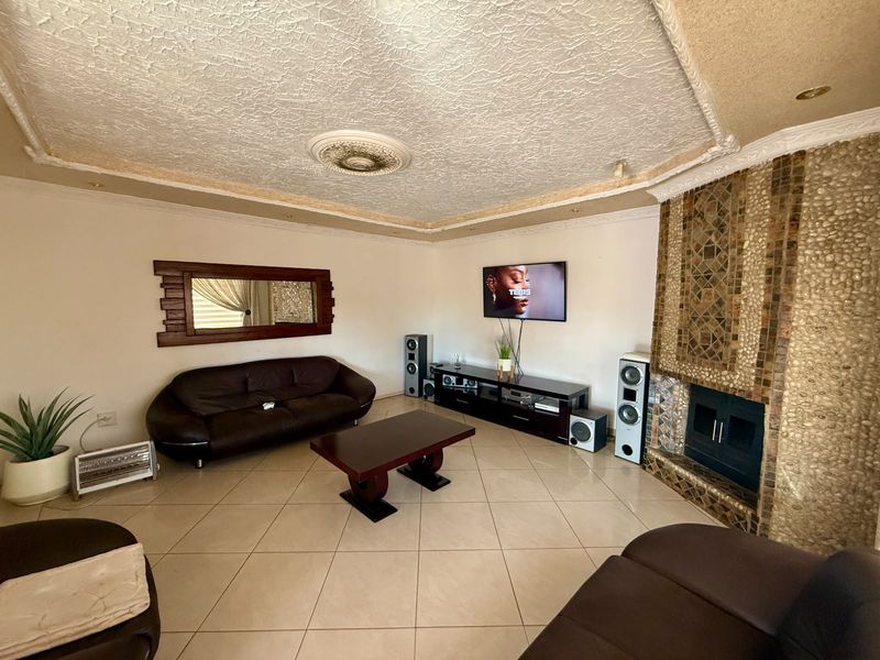Spacious living room featuring a prominent stone-clad built-in fireplace, tiled flooring, and decorative ceiling detailing.