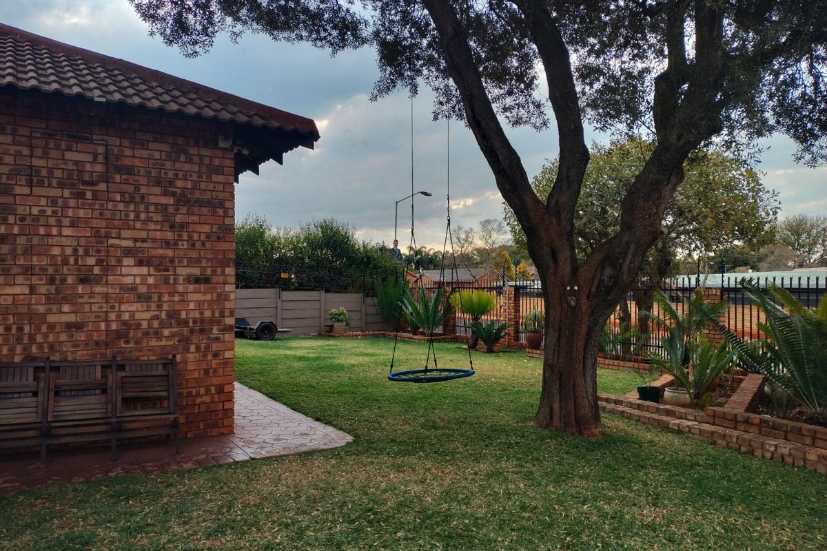 A private rear garden featuring a well-maintained lawn, mature tree, paved patio area, and secure perimeter fencing with face brick exterior walling.