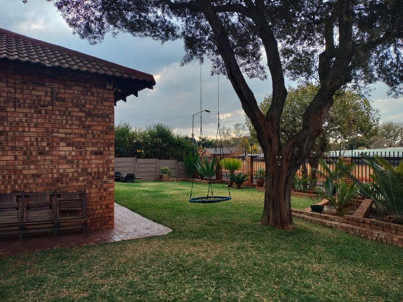 A private rear garden featuring a well-maintained lawn, mature tree, paved patio area, and secure perimeter fencing with face brick exterior walling.