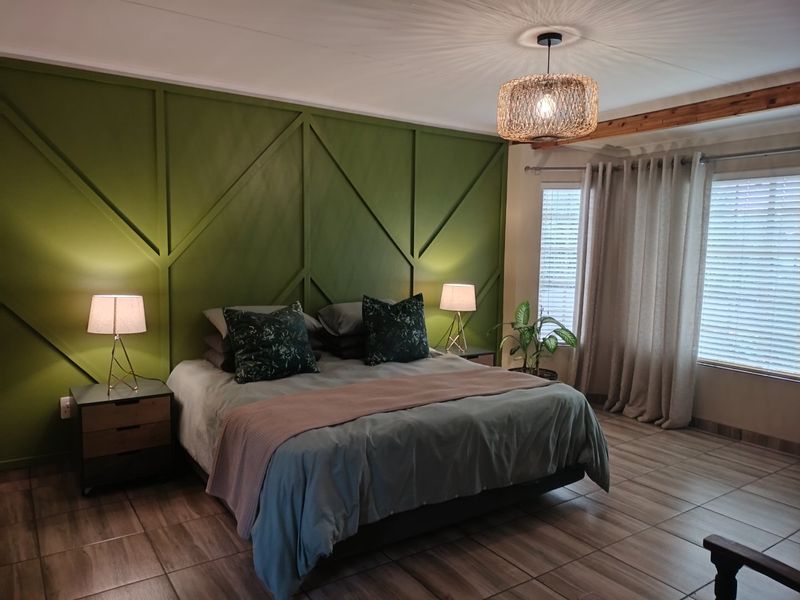 A well-maintained bedroom featuring a decorative green feature wall, tiled flooring, and natural light through venetian blinds.
