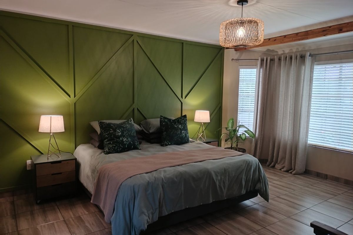 A well-maintained bedroom featuring a decorative green feature wall, tiled flooring, and natural light through venetian blinds.