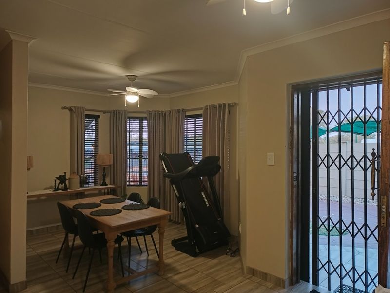 A living area featuring tiled flooring, ceiling fan, and a security gate leading to the exterior.