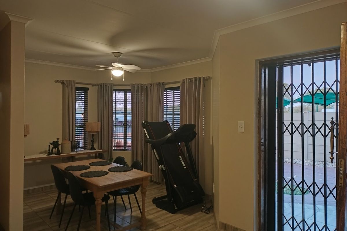 A living area featuring tiled flooring, ceiling fan, and a security gate leading to the exterior.