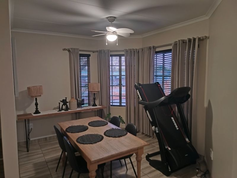 A dining room featuring tiled flooring, a ceiling fan, and large windows with venetian blinds and curtain rods.