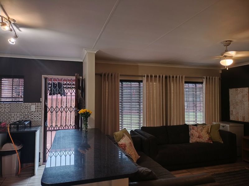 Open plan living area featuring a granite breakfast bar, patterned tile backsplash, ceiling fan, and direct access to the exterior via a security gate.