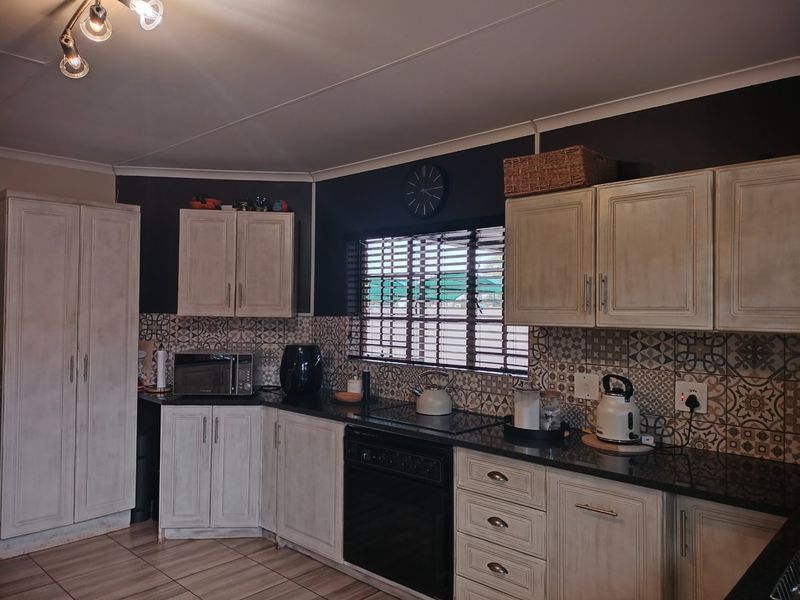 A functional kitchen featuring distressed-finish cabinetry, dark granite countertops, and decorative patterned tile backsplash with integrated oven and hob.