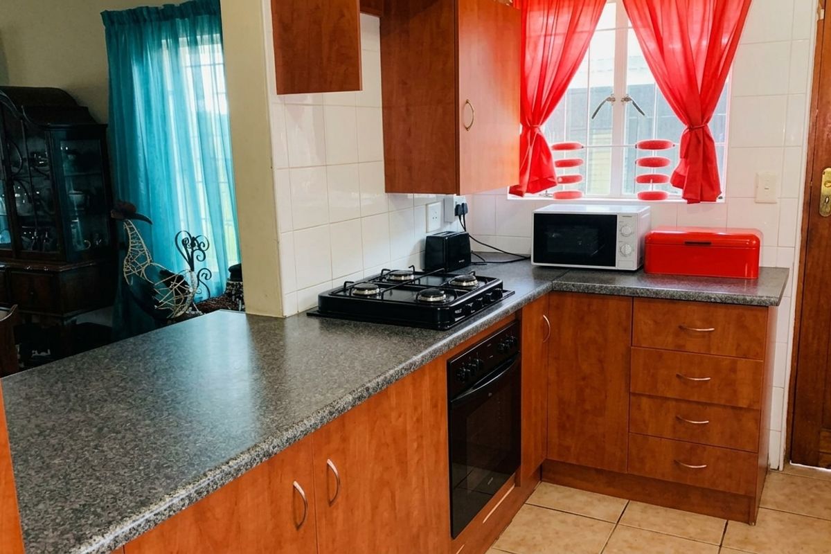 A functional kitchen featuring wood-finish cabinetry, granite-look laminate countertops, a built-in oven with gas hob, and tiled flooring.