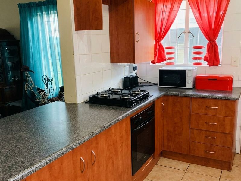 A functional kitchen featuring wood-finish cabinetry, granite-look laminate countertops, a built-in oven with gas hob, and tiled flooring.