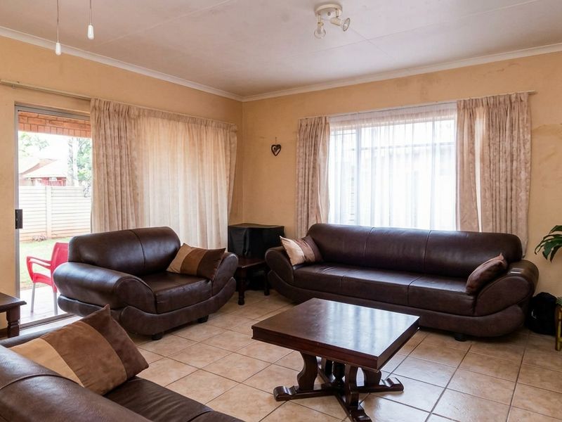 A living room featuring tiled flooring, large windows, and a sliding door leading to the exterior, showing signs of wall wear and staining.