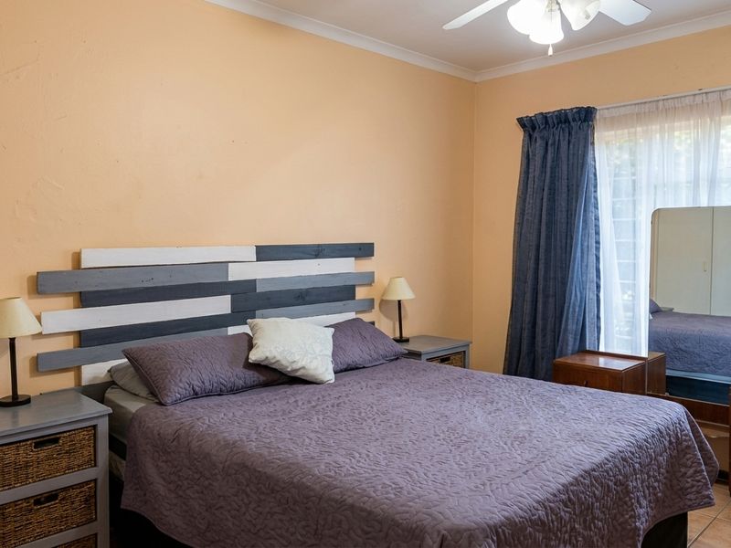 A bedroom featuring tiled flooring and a ceiling fan, with neutral wall tones and natural light provided by a large window.