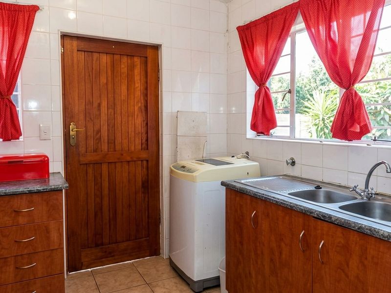 Functional laundry area featuring tiled walls, wooden cabinetry, double stainless steel sink, and direct access to the exterior.
