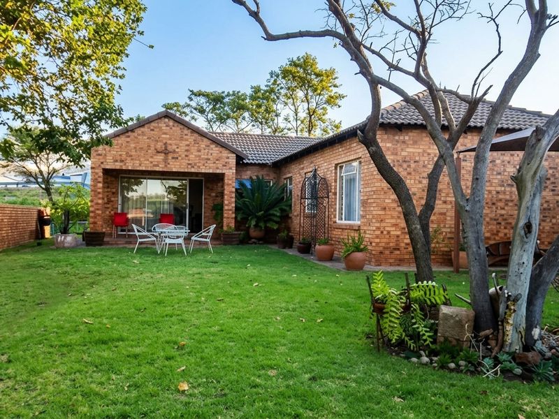 A well-maintained rear exterior view of a face brick house featuring a landscaped garden, paved patio area, and sliding glass door access.