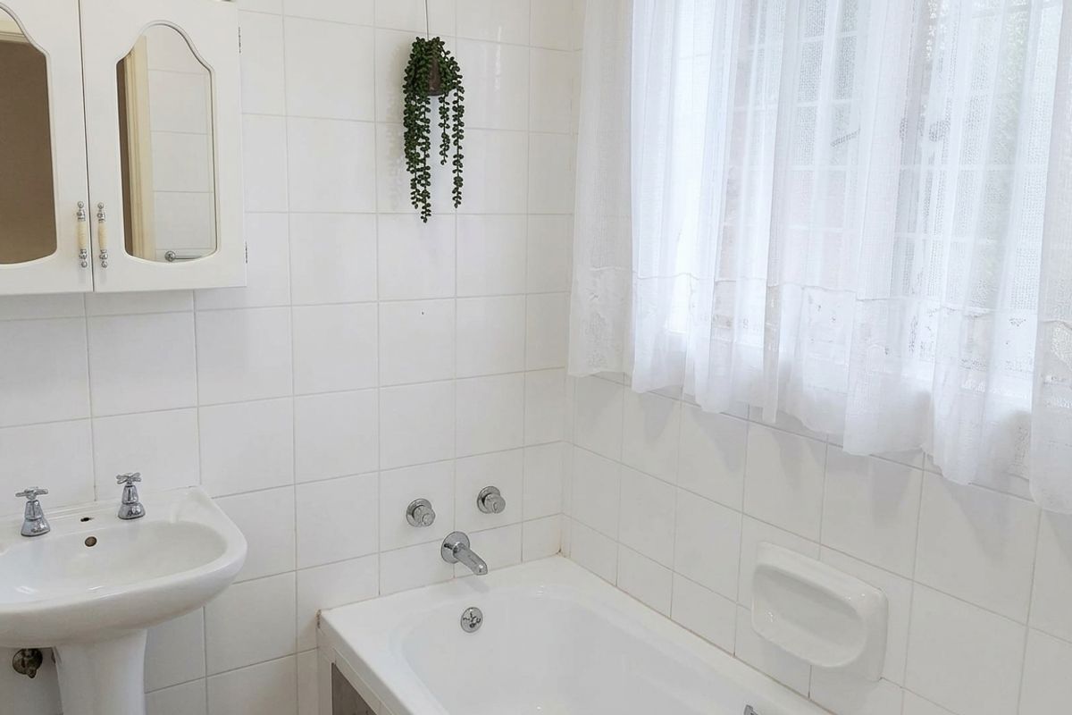 A functional bathroom featuring a pedestal basin, built-in bathtub, and classic white wall tiling, offering a clean and neutral space ready for updates.