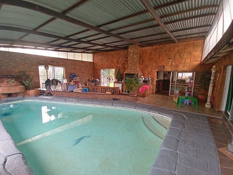 Enclosed indoor pool area featuring a built-in braai, stone-clad walls, and a corrugated metal roof, offering a versatile space for year-round entertainment.
