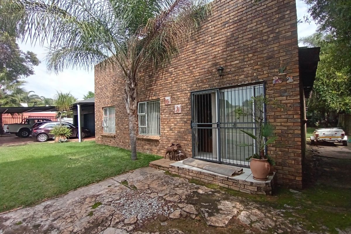 Rear view of a face brick house featuring a paved patio area, sliding glass door with security gate, and adjacent carport.