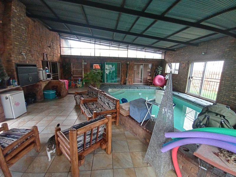 Enclosed indoor pool area featuring a built-in braai, tiled flooring, and exposed brick walls under a high corrugated metal roof.