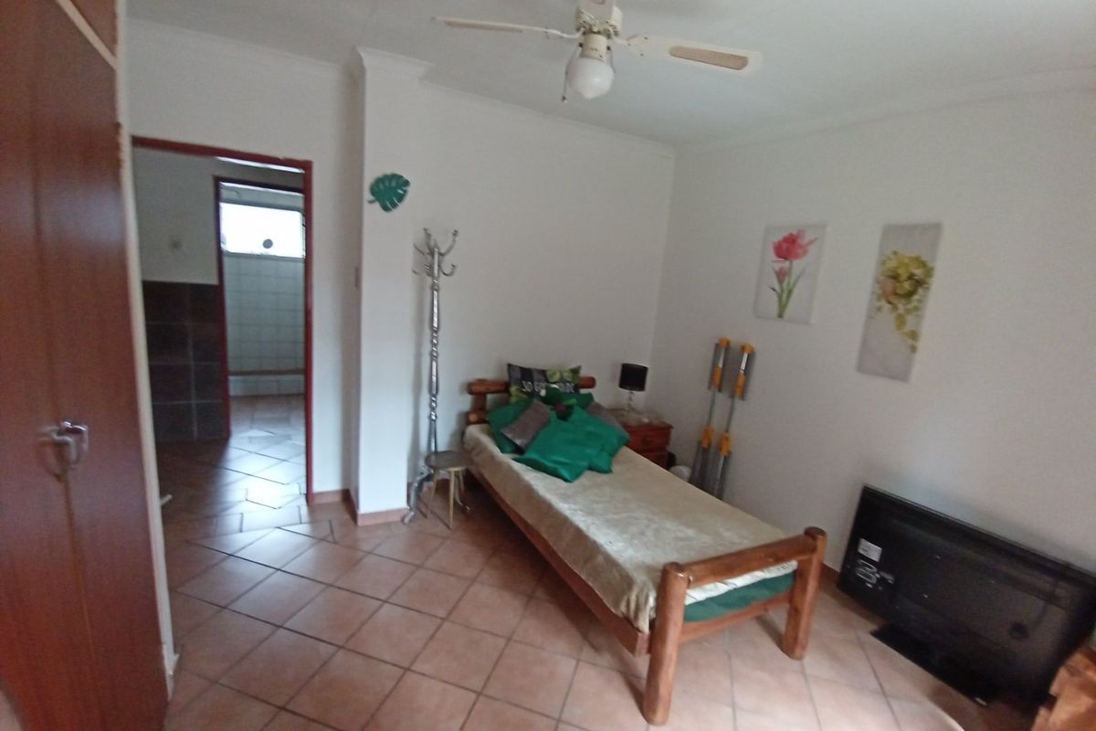 A bedroom featuring tiled flooring, a built-in wardrobe, and a ceiling fan, with an adjoining view into a bathroom area.